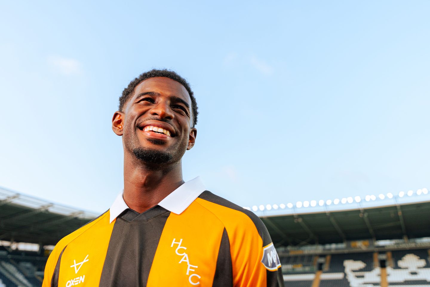 A Hull City player smiling in the club's amber and black striped home shirt